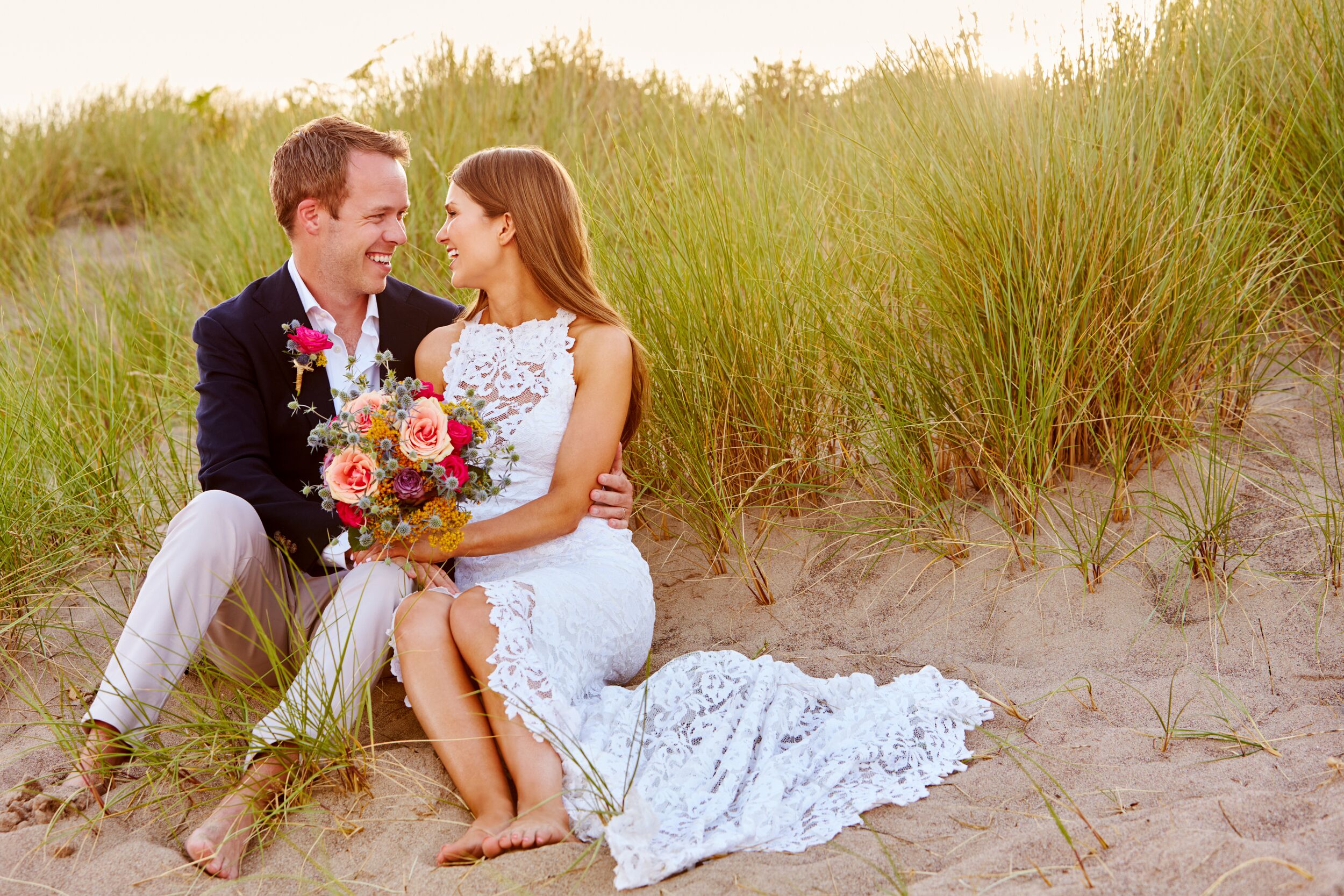 Romantic Married Couple Celebrating Beach Wedding Sitting In Dunes Together